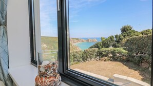 A window with a clear view of a coastal landscape, including rocky cliffs and a body of water. - Beachcomber (Penzance)