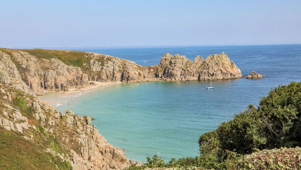 A coastal landscape with rocky cliffs, a beach, and calm sea. - Beachcomber (Penzance)