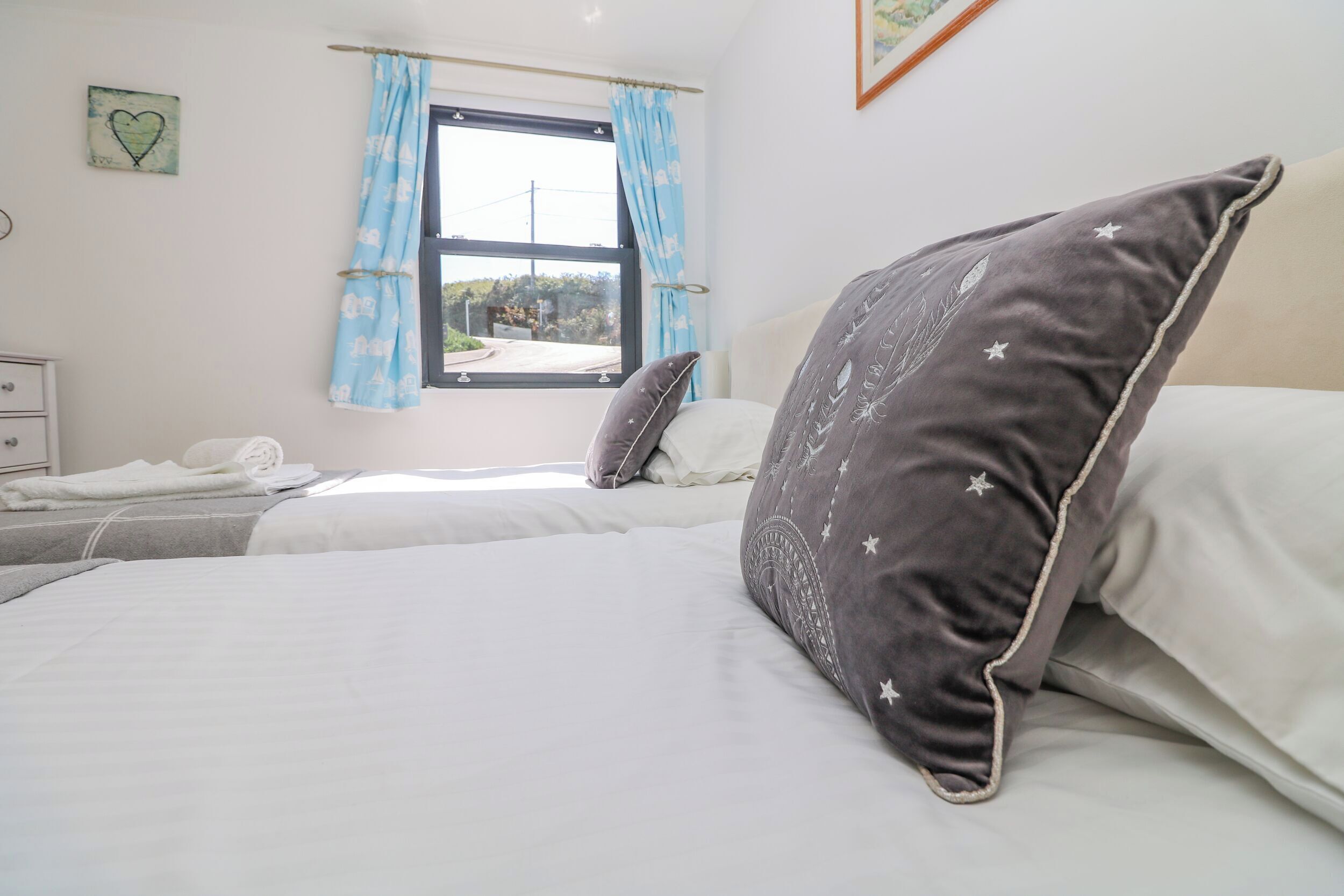 A bedroom with two beds, a window with blue curtains, a dresser, and a heart-shaped decoration on the wall.