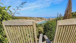 Two wooden chairs facing a scenic coastal view with cliffs and a beach. - Beachcomber (Penzance)