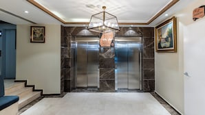 A modern lobby with a marble floor, a geometric chandelier, and two elevators. - Ain Benian (Algiers)
