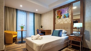 A hotel room with a large bed, a wooden nightstand, a desk, a chair, a potted plant, and a painting on the wall. - Ain Benian (Algiers)