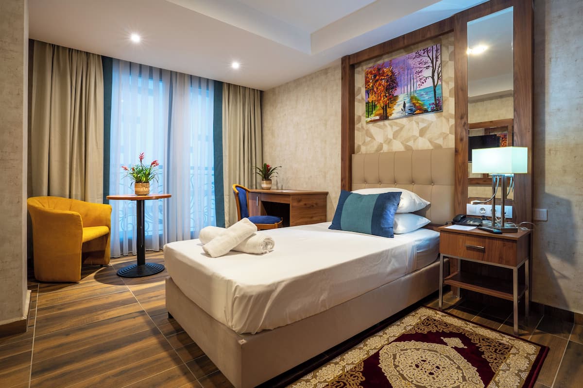 A hotel room with a large bed, a wooden nightstand, a desk, a chair, a potted plant, and a painting on the wall.