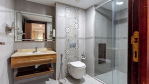 A modern bathroom with a wooden vanity, a glass shower enclosure, and patterned tiles. - Ain Benian (Algiers)