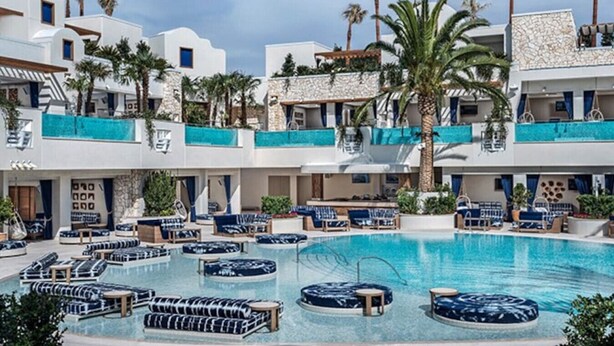 Ein Poolbereich mit Liegestühlen und einem klaren, blauen Pool, umgeben von mehrstöckigen Gebäuden mit Balkonen und Palmen.