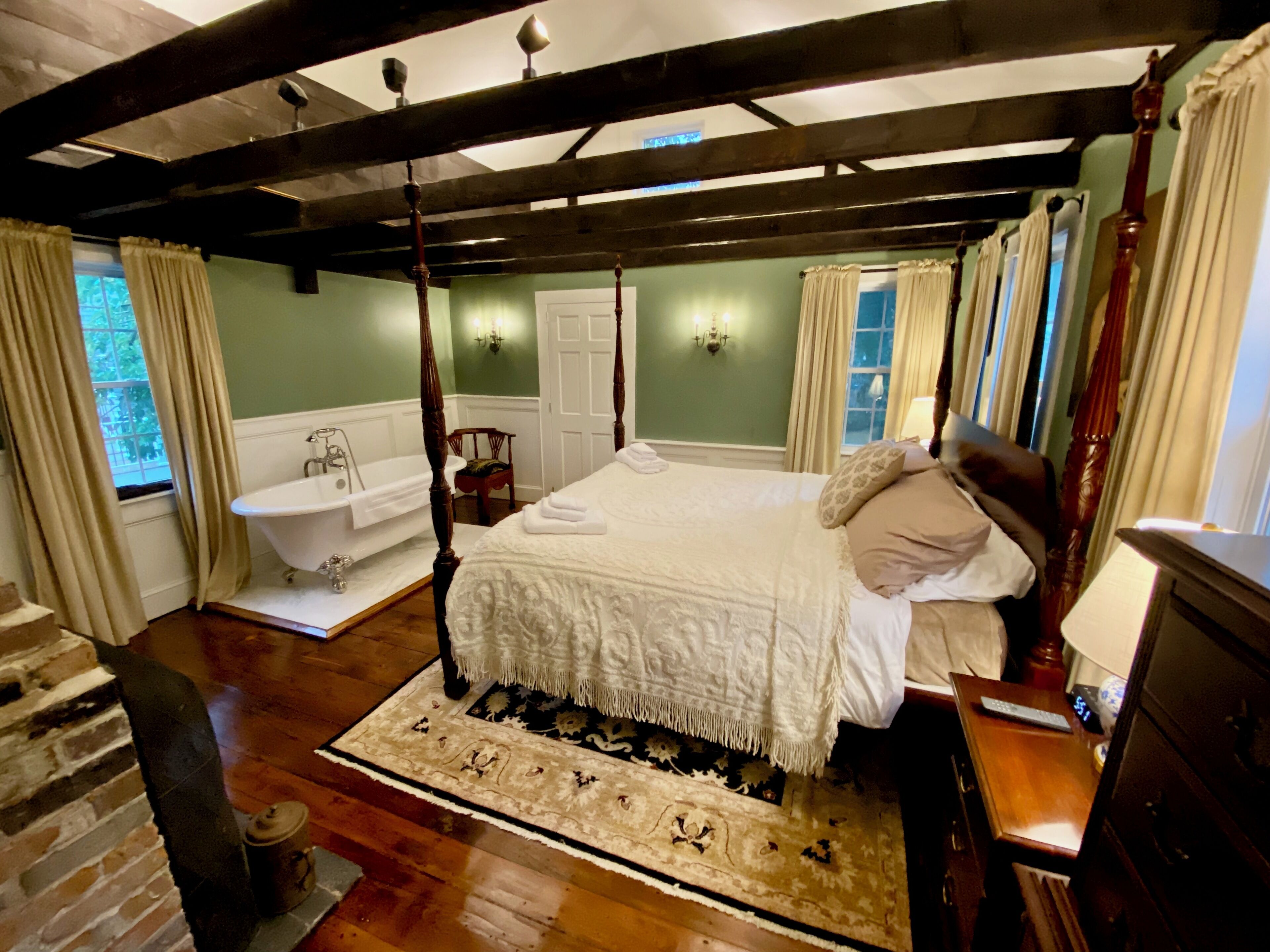 A bedroom with a four-poster bed, a clawfoot bathtub, and a wooden floor.