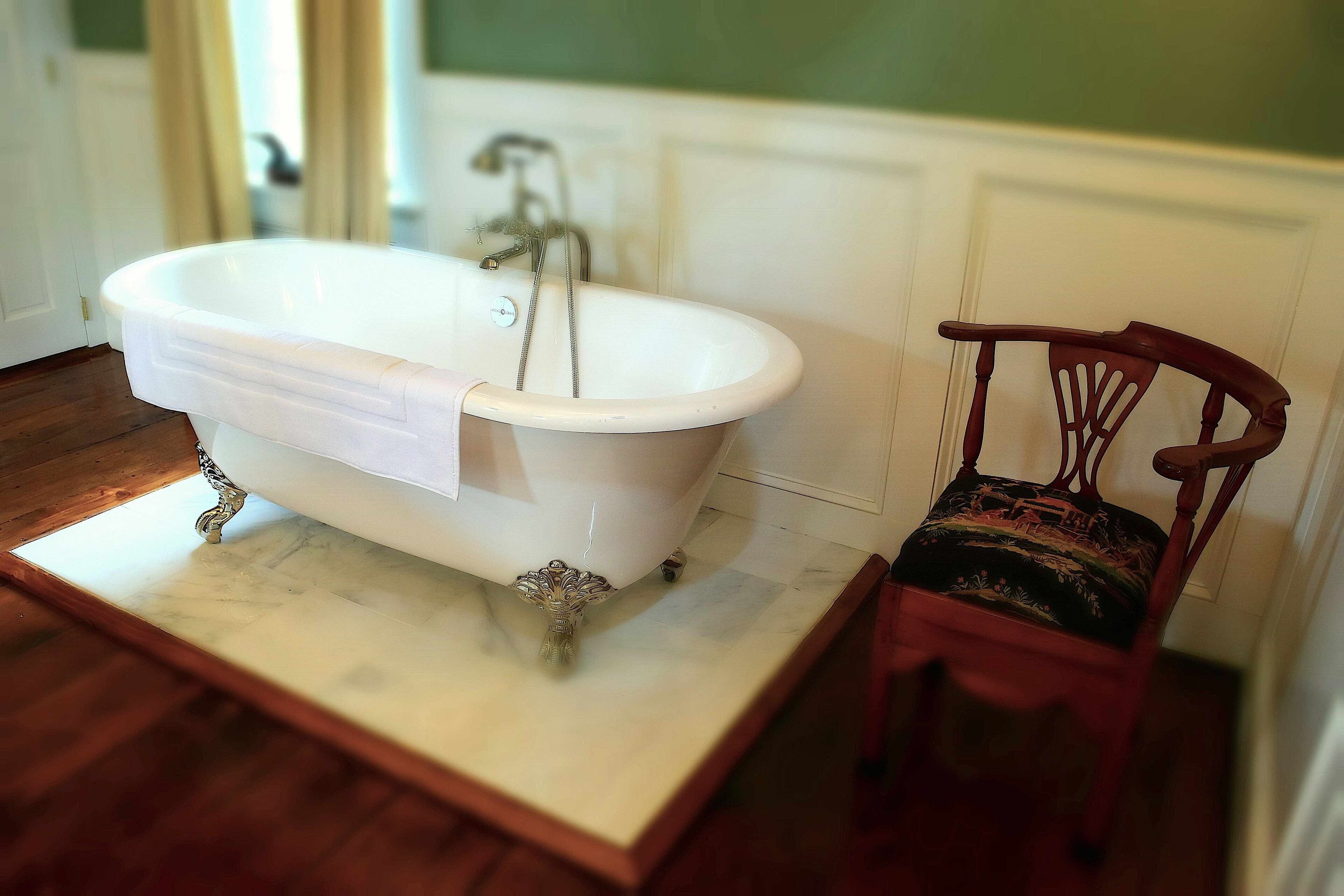A bathroom with a freestanding bathtub, a wooden chair with a patterned cushion, and a marble countertop.