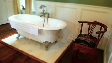 A bathroom with a freestanding bathtub, a wooden chair with a patterned cushion, and a marble countertop.