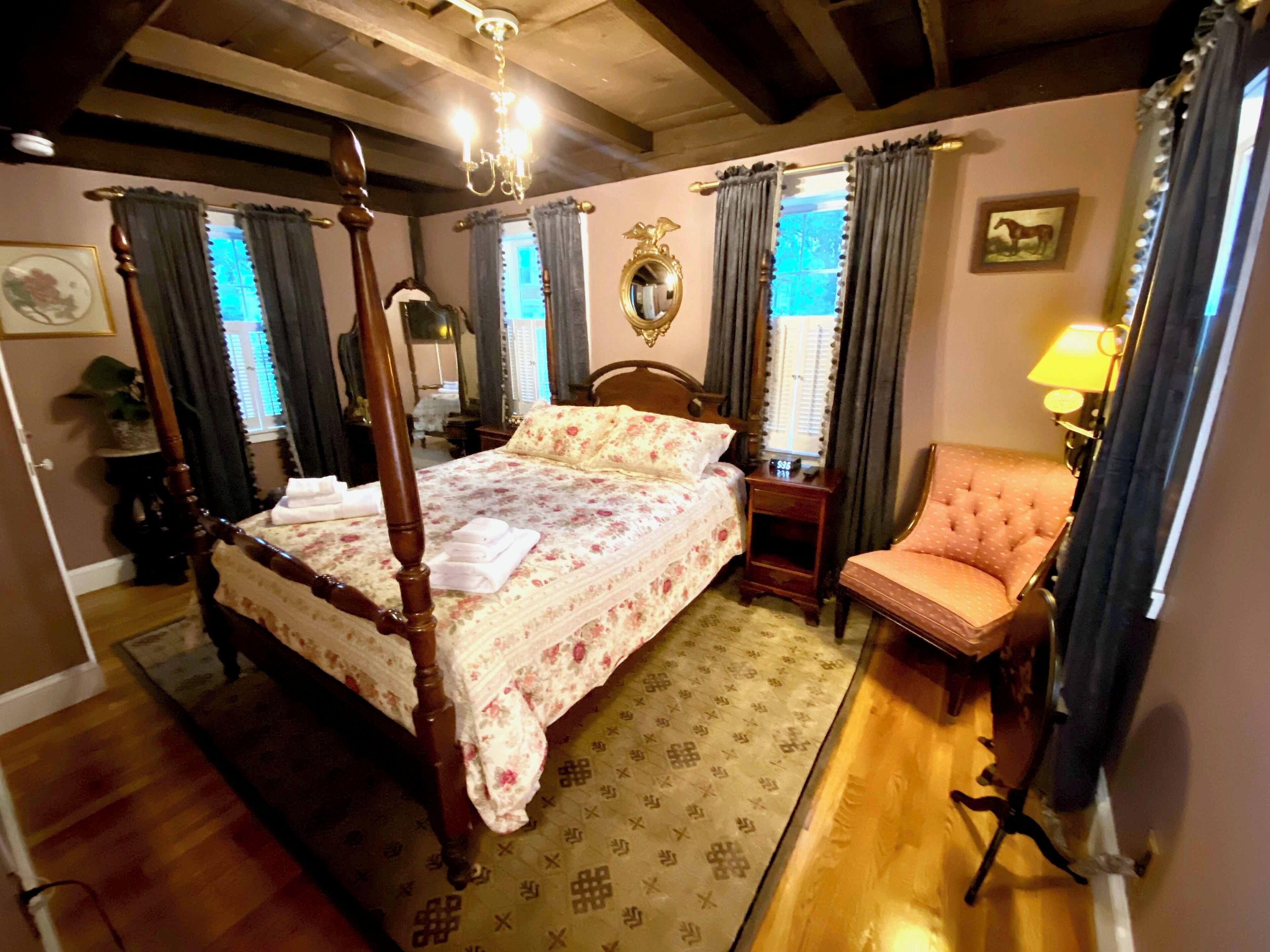 A traditional bedroom with a four-poster bed, a wooden chair, a small table, and a mirror on the wall.