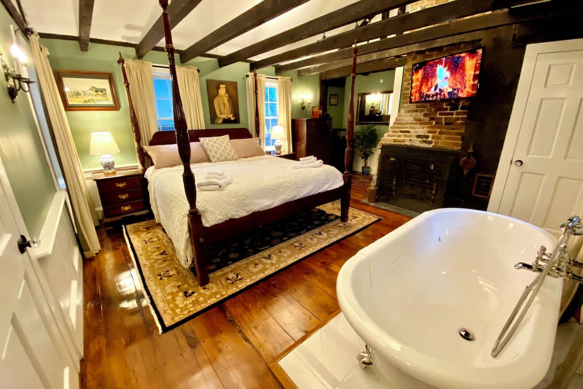 A bedroom with a four-poster bed, a large white bathtub, and a stone fireplace.