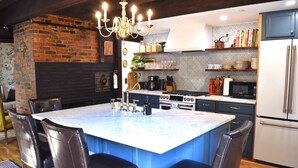 A modern kitchen with a central island, dark cabinetry, and a brick accent wall. - Silsbee's by Daniels House (Salem)