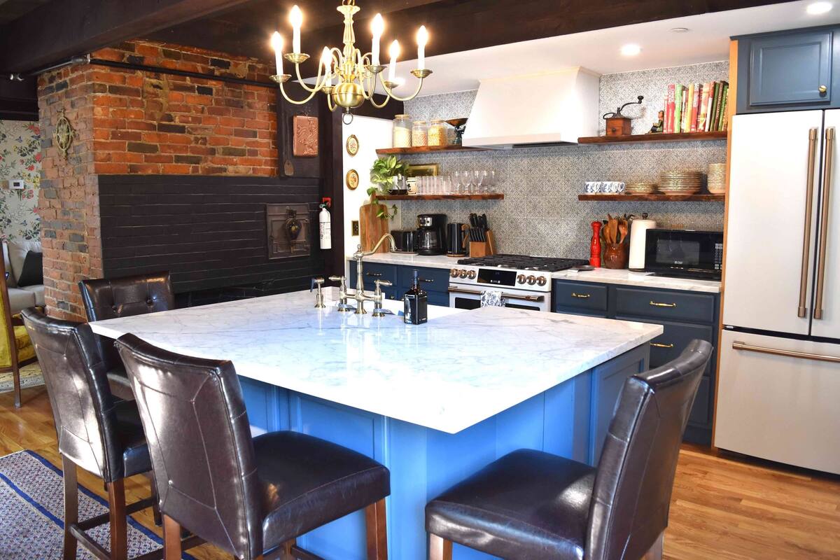 A modern kitchen with a central island, dark cabinetry, and a brick accent wall.