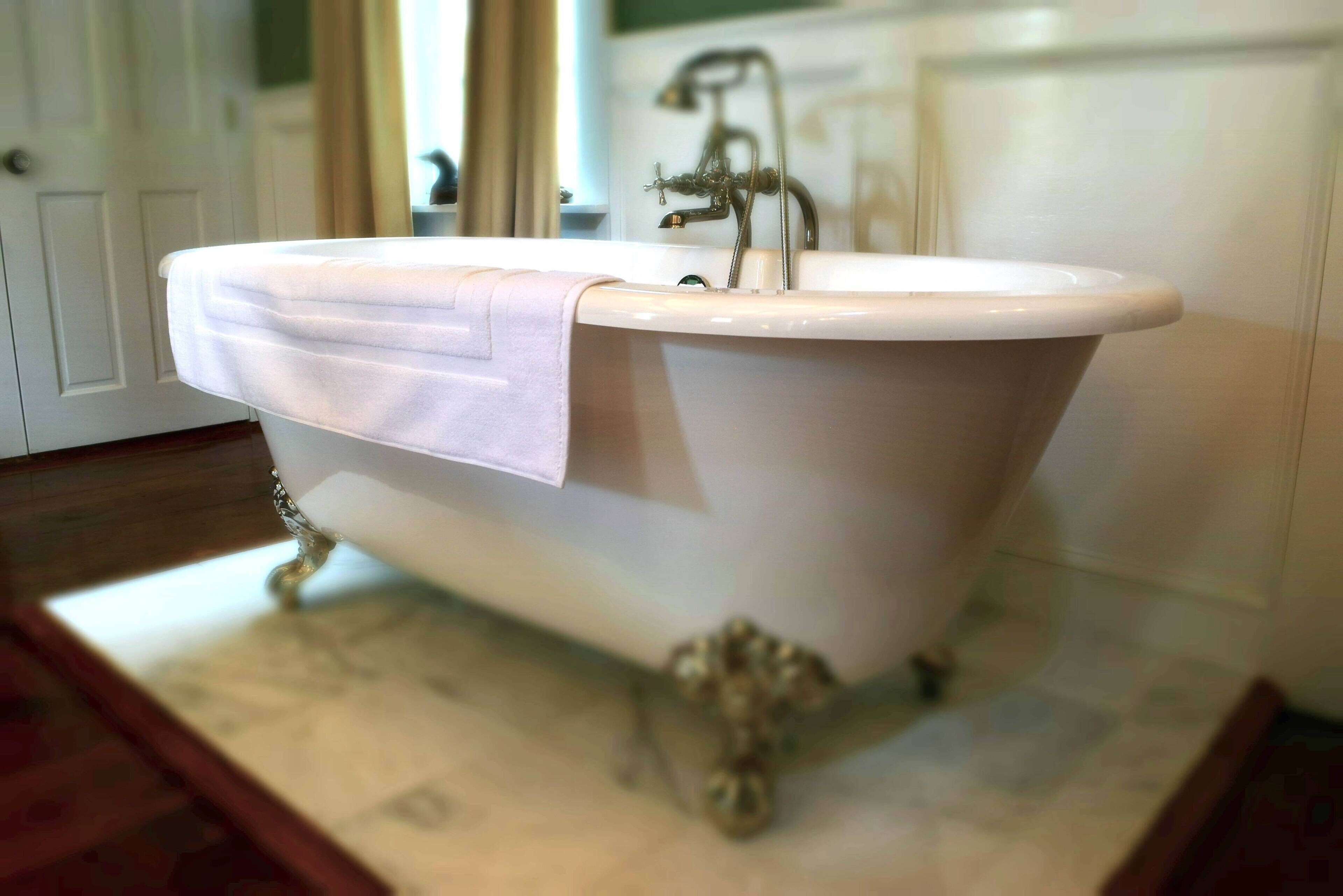 A white freestanding bathtub with a single faucet and a towel draped over it.