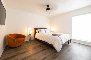 A bedroom with a bed, a chair, a bedside table, and a ceiling fan.