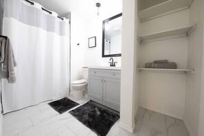 A bathroom with a toilet, a sink, a mirror, a shower curtain, and a black rug. - The Grand Escape: 4 Bedroom, 1 Story Home (The Colony)