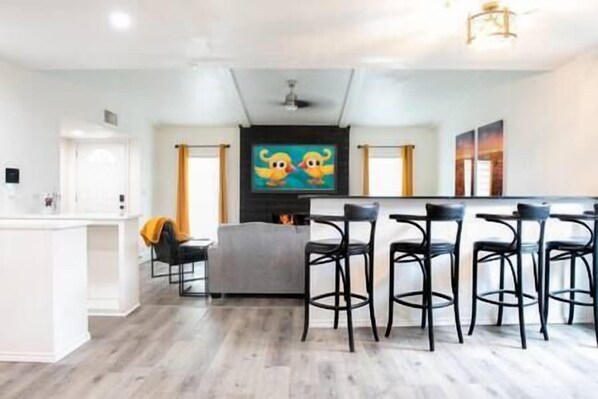 A modern kitchen with a central island, bar stools, and a large TV screen displaying a cartoon.
