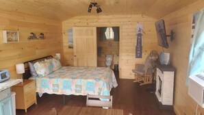 A cozy wooden cabin room with a bed, a small desk, a chair, a fan, and a sign that reads "WELCOME". -  Lighthouse Cabins Maine (Bass Harbor)