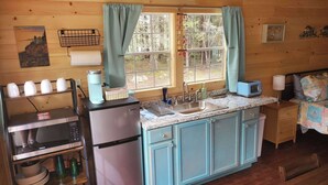 A compact kitchen with a refrigerator, microwave, and sink. There is a small dining area with a table and chairs. -  Lighthouse Cabins Maine (Bass Harbor)