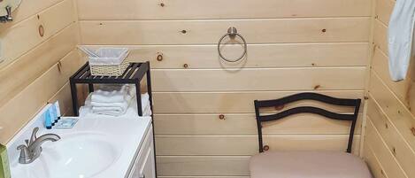 Un baño con pared de madera, un lavamanos, un inodoro, una silla y una alfombra azul.