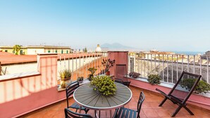 A terrace with a round table and chairs, potted plants, and a view of the sea and buildings. - Dream Terrace on the Gulf (Naples)