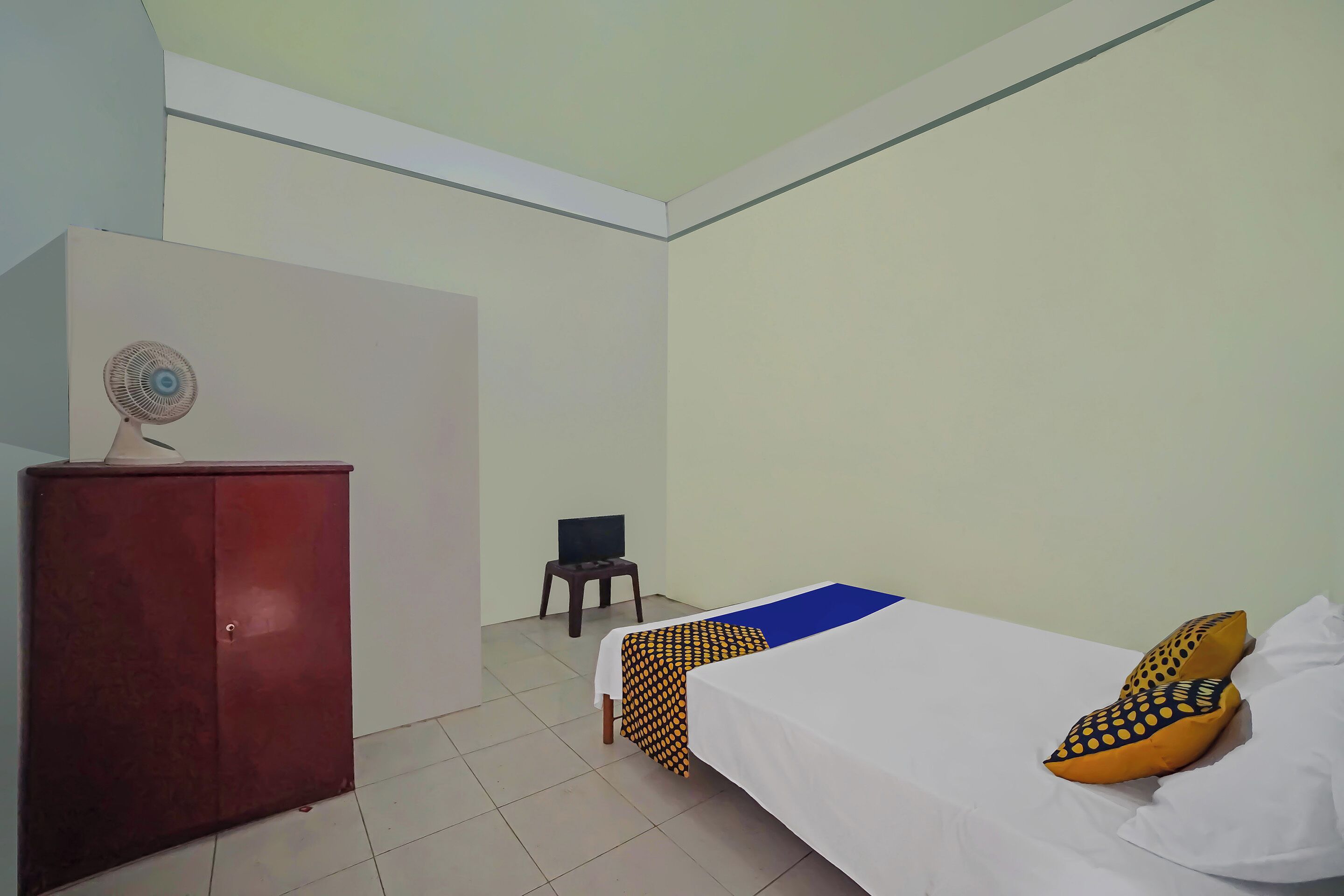 A room with a bed, a red cabinet, a small table with a TV, and a fan.