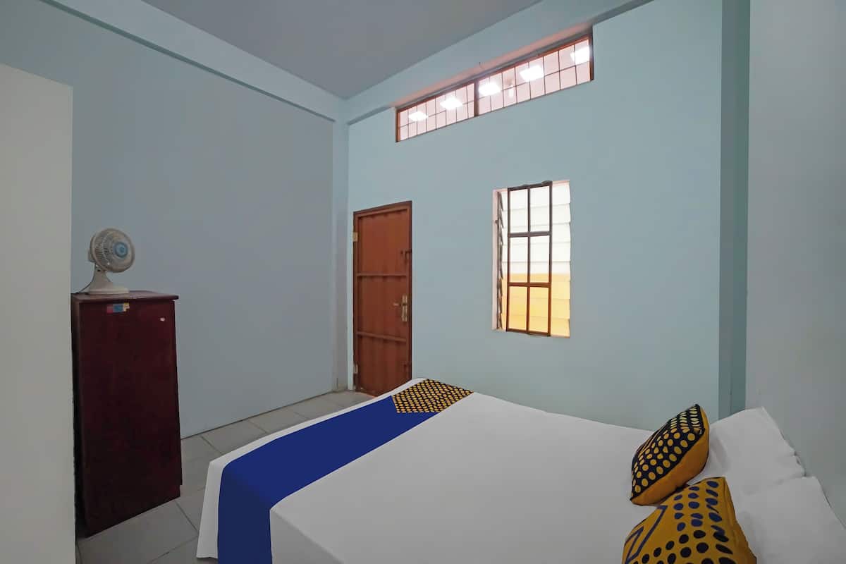 A room with a bed, a desk, and two windows.