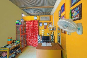 Ein Zimmer mit einem Holztisch, einem Ventilator, einem Fernseher und einem Bücherregal.