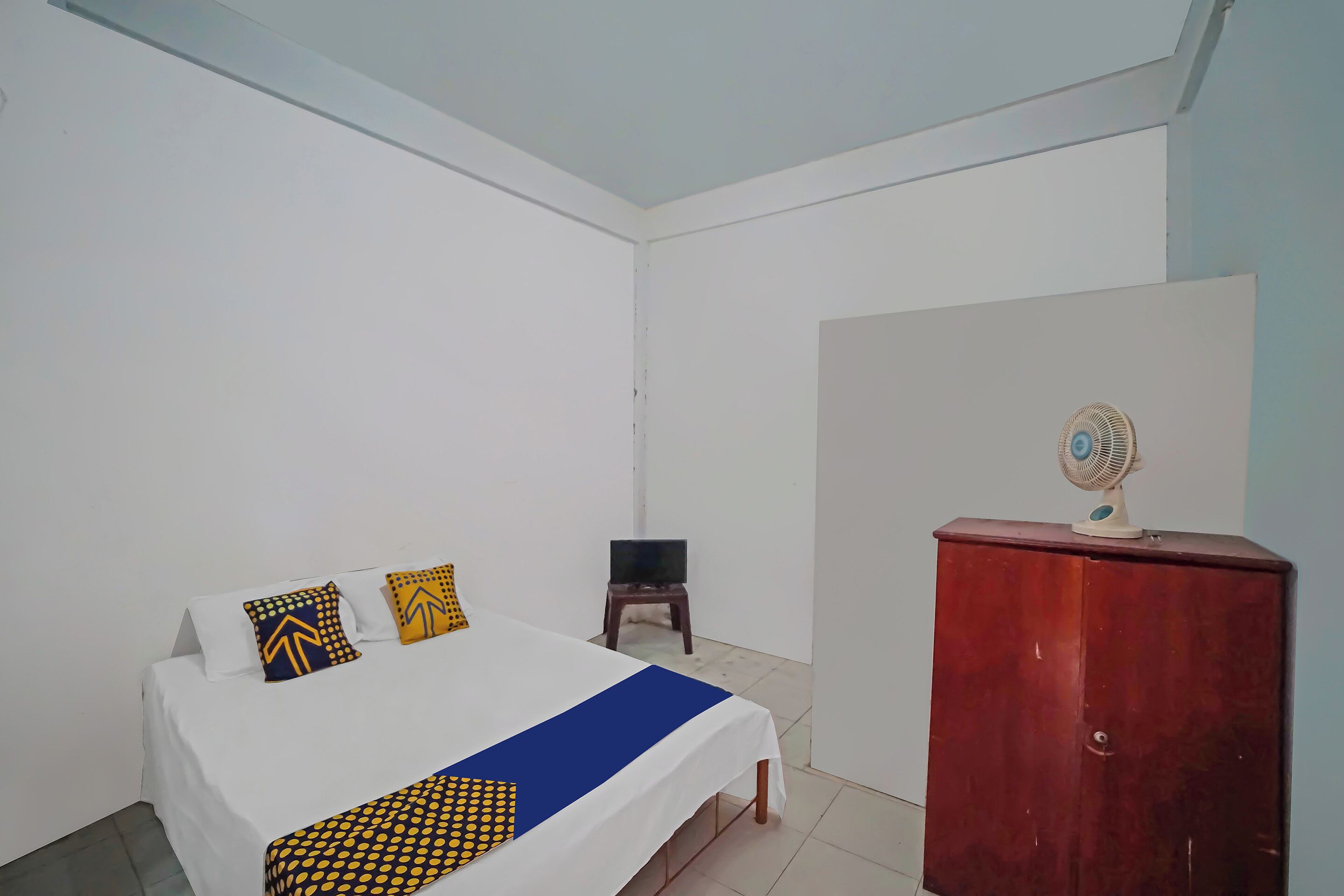 Quarto com cama, armário de madeira e uma mesinha com televisão.
