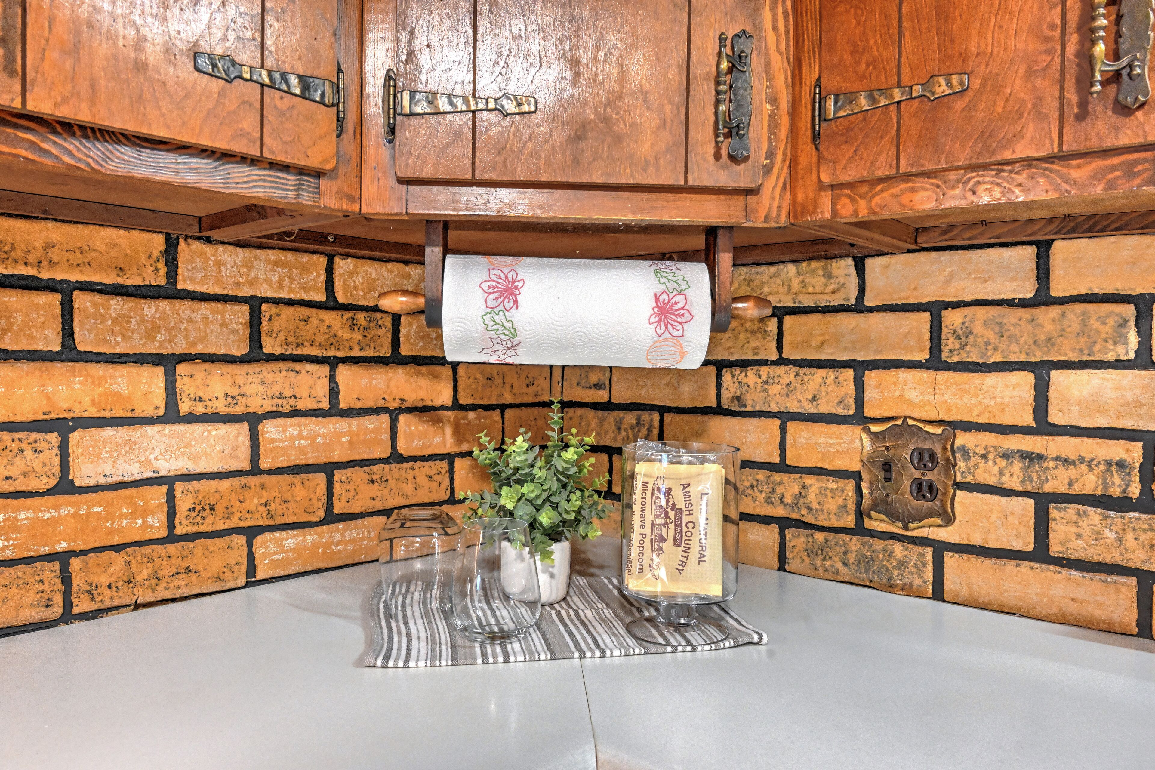 Una cocina con armarios de madera, pared de ladrillo, encimera, un rollo de toallas de papel, una planta en maceta y un microondas.