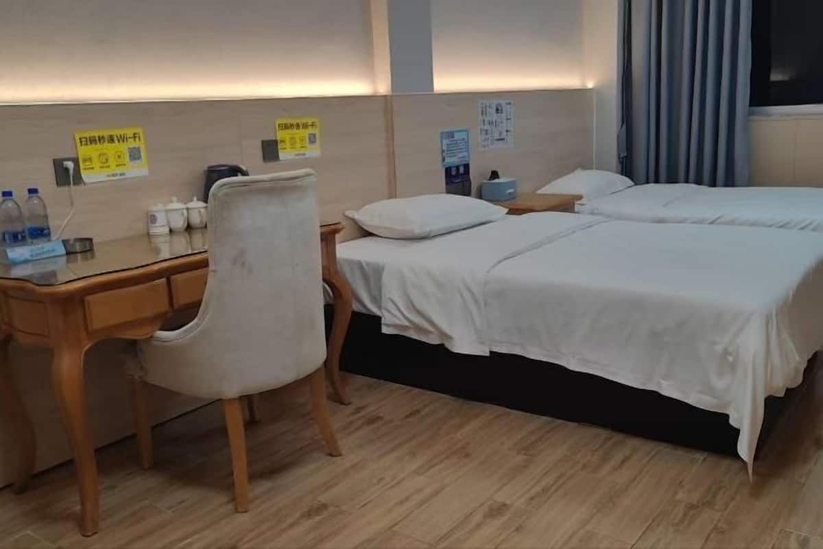 A hotel room with a desk, chair, two beds, and a nightstand.