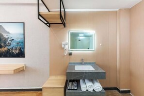 A modern bathroom with a marble sink, a mirror with backlighting, a wooden bench, and a framed coastal landscape picture on the wall.