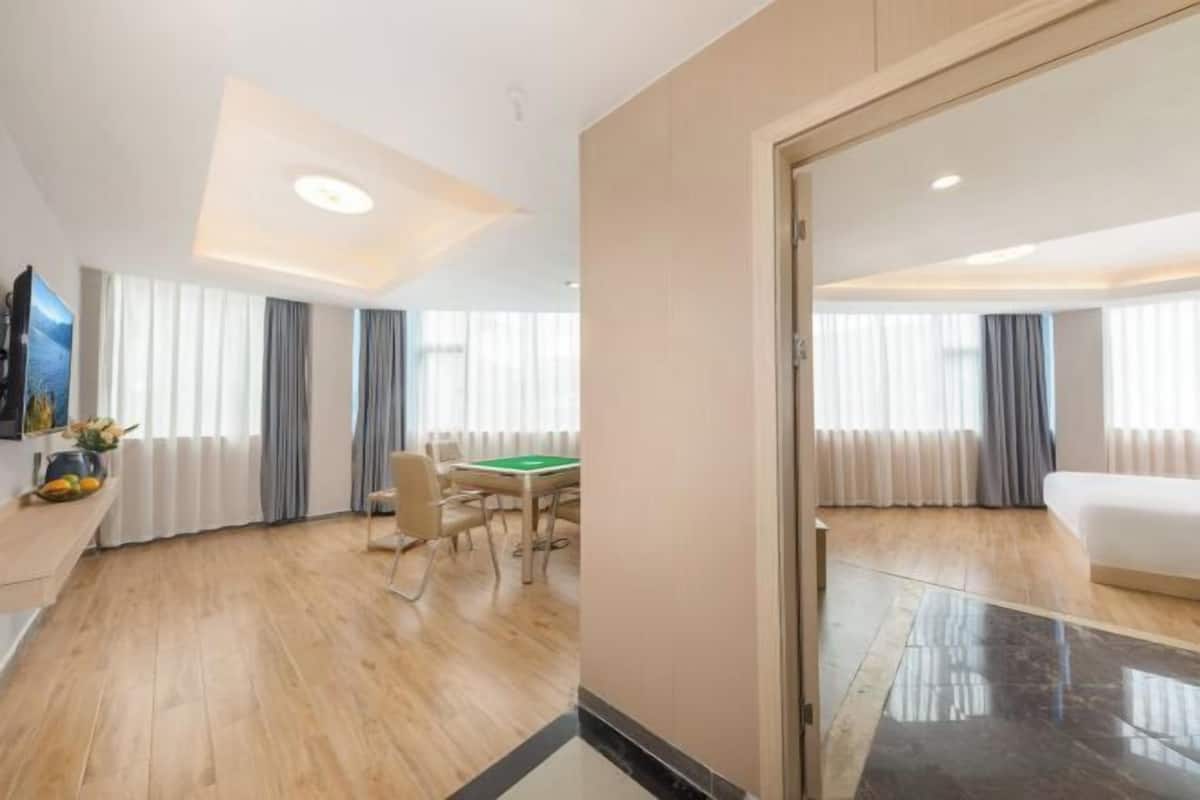 A hotel room with a wooden floor, a dining table with chairs, a bed, and a television.