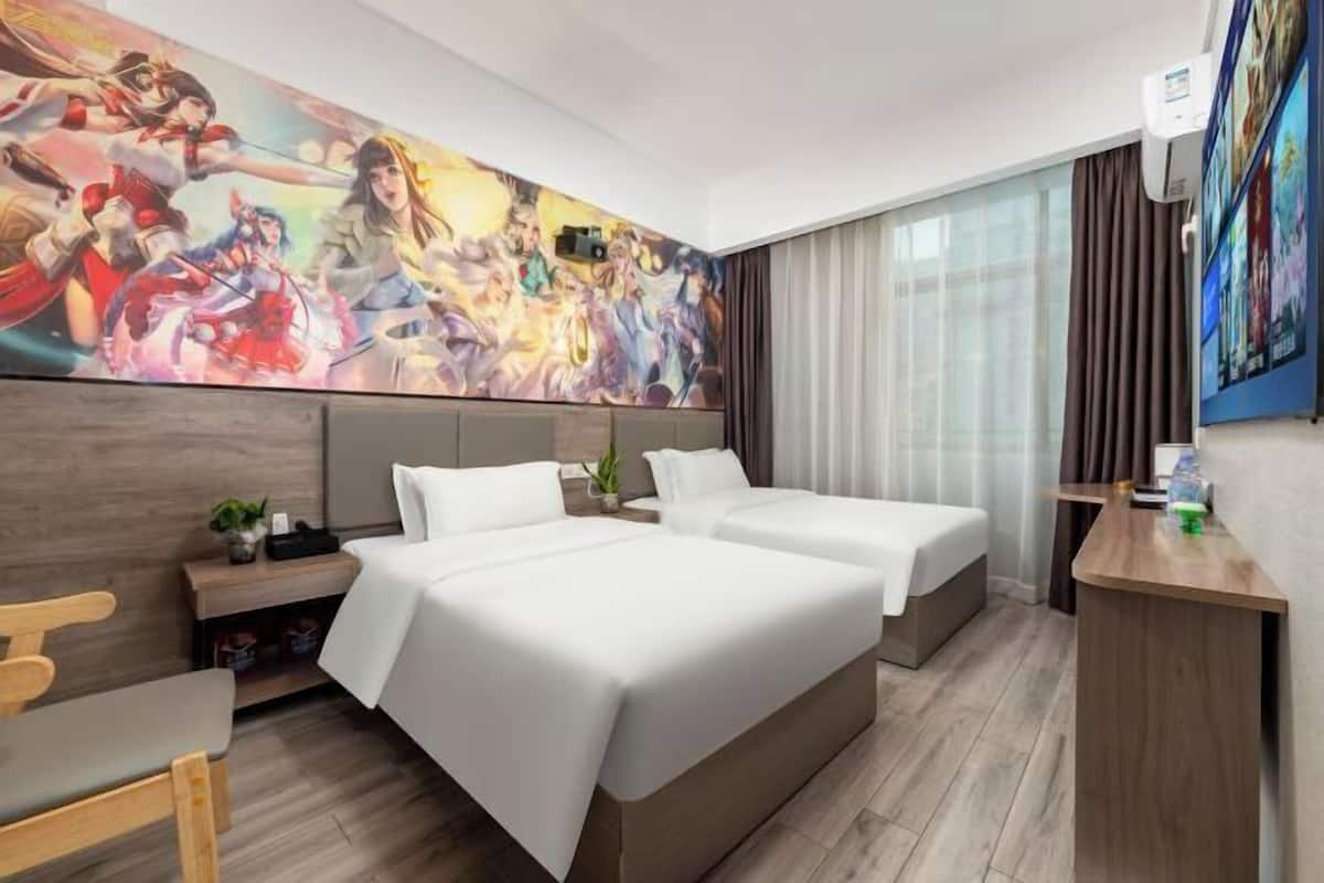A hotel room with two beds, a desk, a chair, a large mural, and a window with curtains.