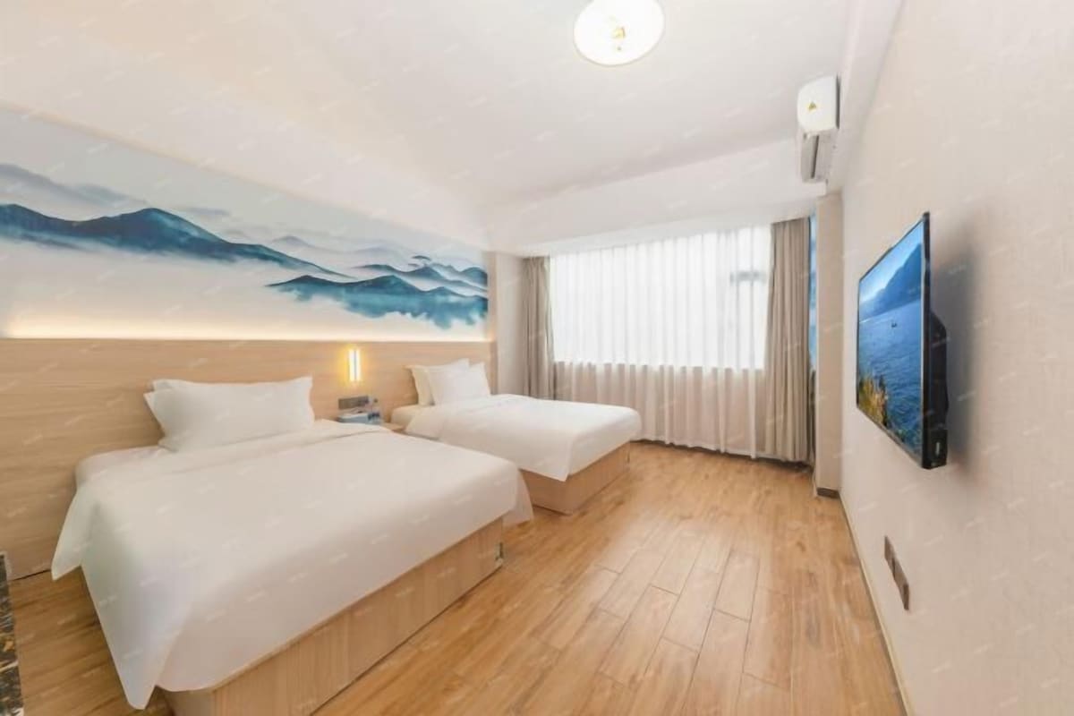 A hotel room with two beds, a large painting on the wall, a TV on the wall, and a window with curtains.