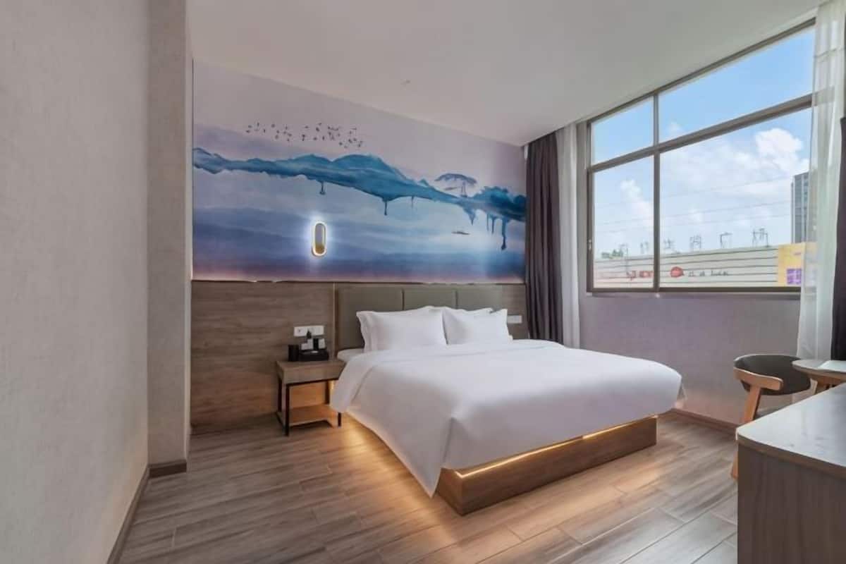 A hotel room with a bed, bedside tables, a desk, a large window, and a wall mural.