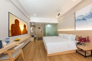 A modern hotel room with a large bed, a desk with a chair, a mirror, and artwork on the walls.