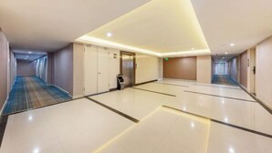 Un couloir d’hôtel au design moderne, avec un luminaire central, une poubelle et un ascenseur bien visible.