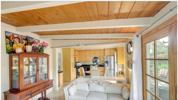 A spacious living area with a wooden ceiling, a white sofa, a wooden cabinet with glass doors, and a kitchen in the background. - Sunny San Diego La Mesa Charming 2 bd /1 bth Home, Beaches, Sea World, Zoo, (La Mesa)