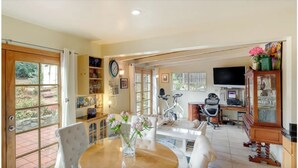 A spacious living area with a dining table, chairs, a sofa, a TV, a bicycle, and a cabinet with decorative items. - Sunny San Diego La Mesa Charming 2 bd /1 bth Home, Beaches, Sea World, Zoo, (La Mesa)