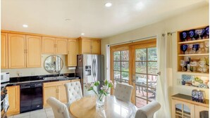 A kitchen with wooden cabinets, a stainless steel refrigerator, a dining table with chairs, and a window with a view of the outdoors. - Sunny San Diego La Mesa Charming 2 bd /1 bth Home, Beaches, Sea World, Zoo, (La Mesa)