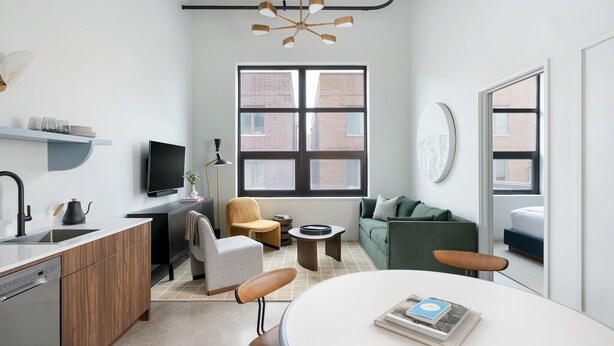 A modern apartment with a kitchen, dining area, and living room. It features a large window, a flat-screen TV, and a ceiling light fixture.