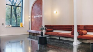 A modern lobby with a large window, a red sofa, a round table, and a bench.