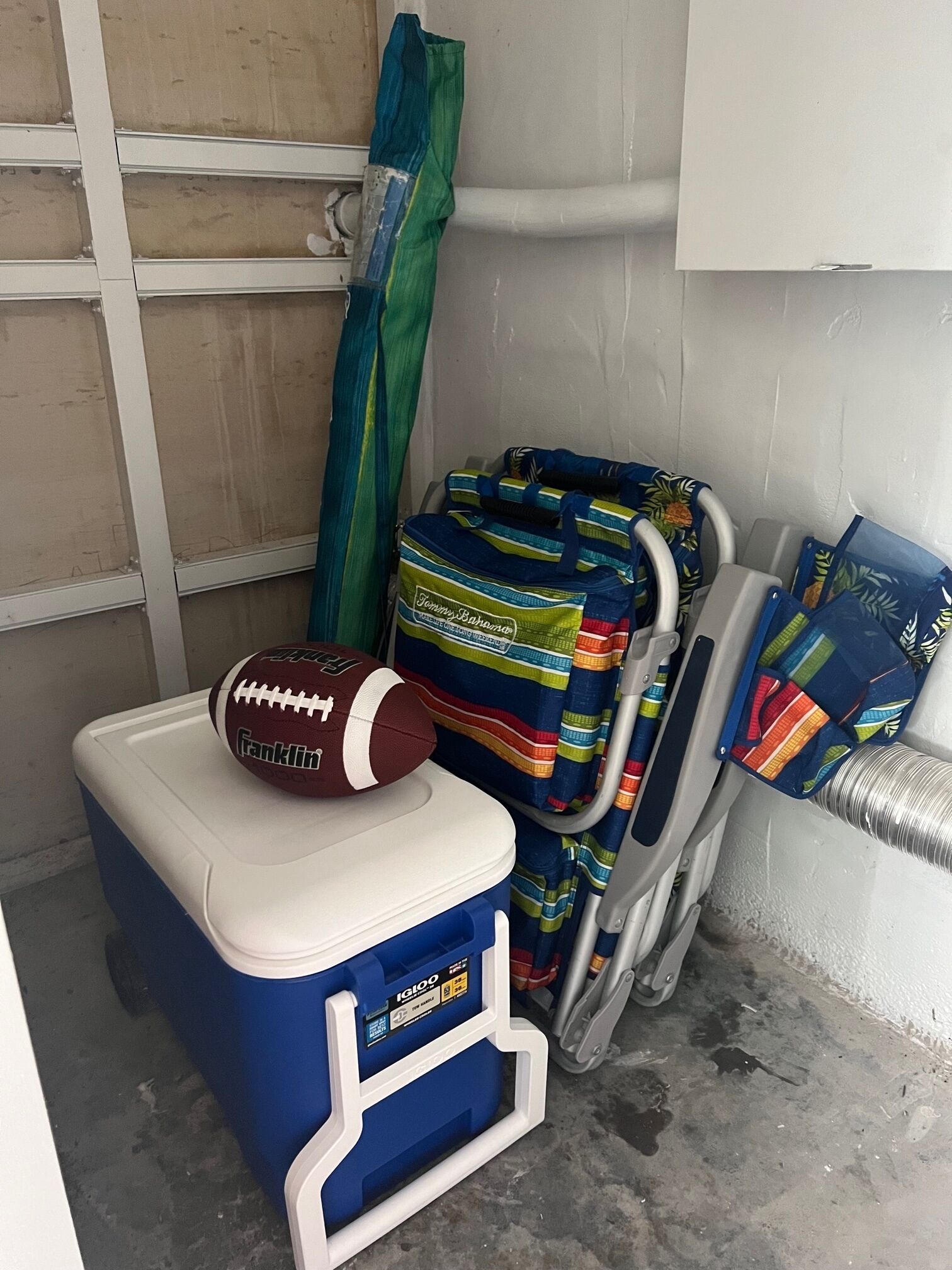 A small room with a blue cooler, a football, and colorful bags.