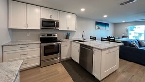 A modern kitchen with white cabinets, stainless steel appliances, a marble countertop, and a built-in dishwasher. - Blue Water Retreat @ Vanderbilt- steps to beaches/shopping/dining/entertainment! (Naples)