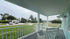 A porch with a white railing, a wooden deck, and a view of a street with parked cars and houses. - Blue Water Retreat @ Vanderbilt- steps to beaches/shopping/dining/entertainment! (Naples)