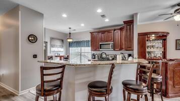 A modern kitchen with a central island, wooden bar stools, and built-in appliances.