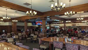 A spacious restaurant with high ceilings, wooden paneling, and multiple chandeliers. Tables are arranged in a casual layout, and a television is mounted on the wall. - Myrtle Beach Legends Golf Condo, on course! 3BR/2BA, pool, hot tub, and tennis. (Myrtle Beach)