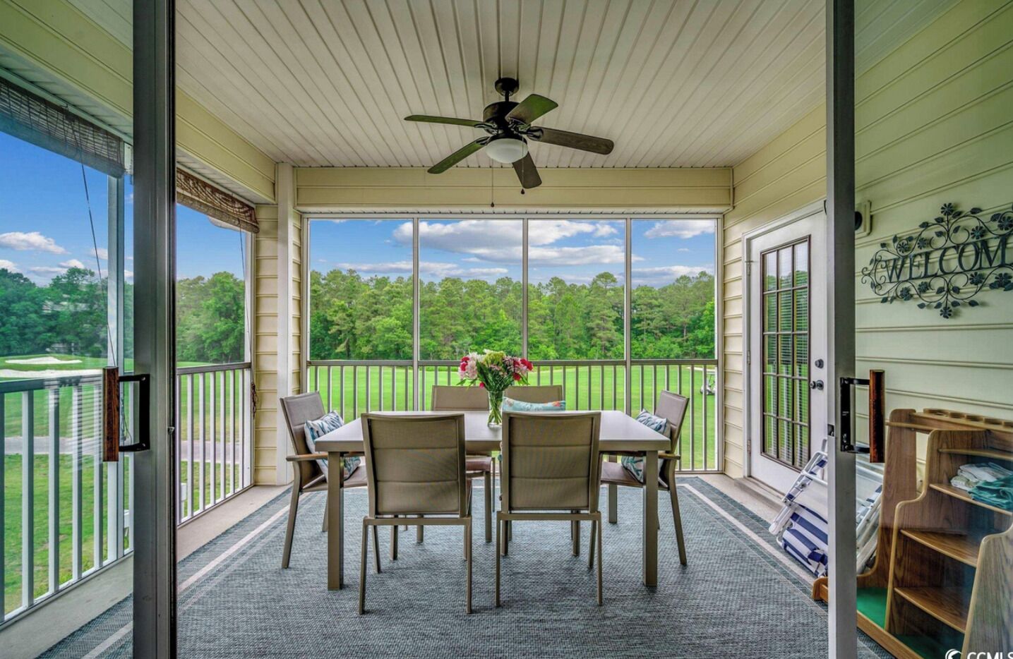 A covered patio with a table and chairs, a ceiling fan, and a view of a green landscape.