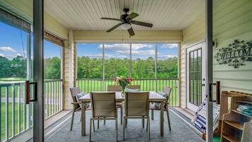 A covered patio with a table and chairs, a ceiling fan, and a view of a green landscape.