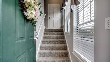 A staircase with a green door, a white door, and a window with blinds.